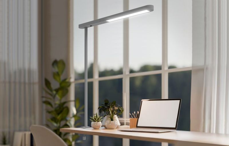A linear desk luminaire above a laptop and a light wood worktop